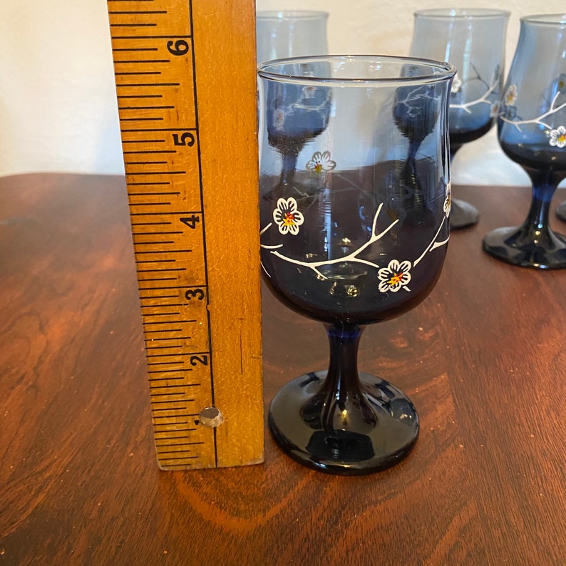May include: Set of four blue glass wine glasses with white floral designs. The glasses have a stem and a round base.