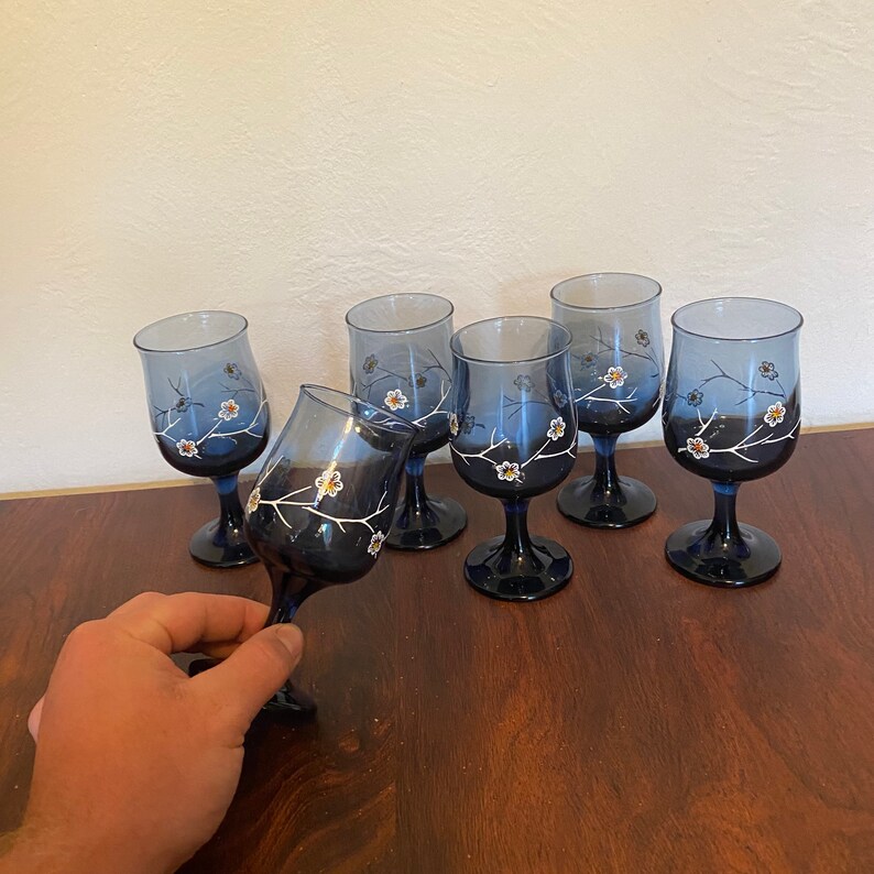 May include: Set of six blue glass wine glasses with white floral designs. The glasses have a clear base and a round bowl.