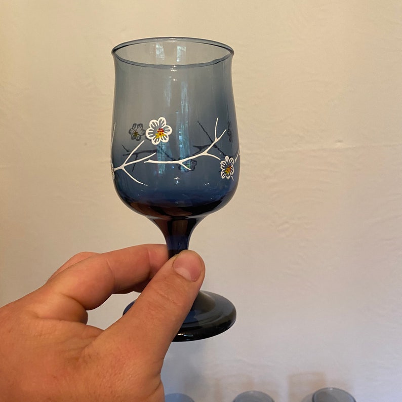 May include: A blue glass wine glass with a white floral design. The glass has a stem and a round base.