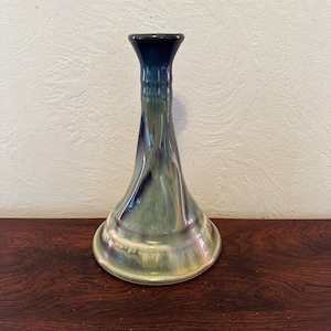 May include: A ceramic candlestick with a green and blue glaze. The candlestick has a wide base and a narrow neck.