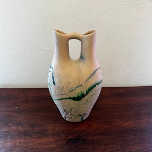 May include: A beige ceramic vase with a unique double-spout design. The vase is decorated with green and blue marbling.