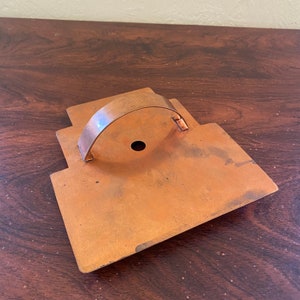 May include: A copper cookie cutter in the shape of a house with a handle. The cutter has a hole in the center and is slightly tarnished.