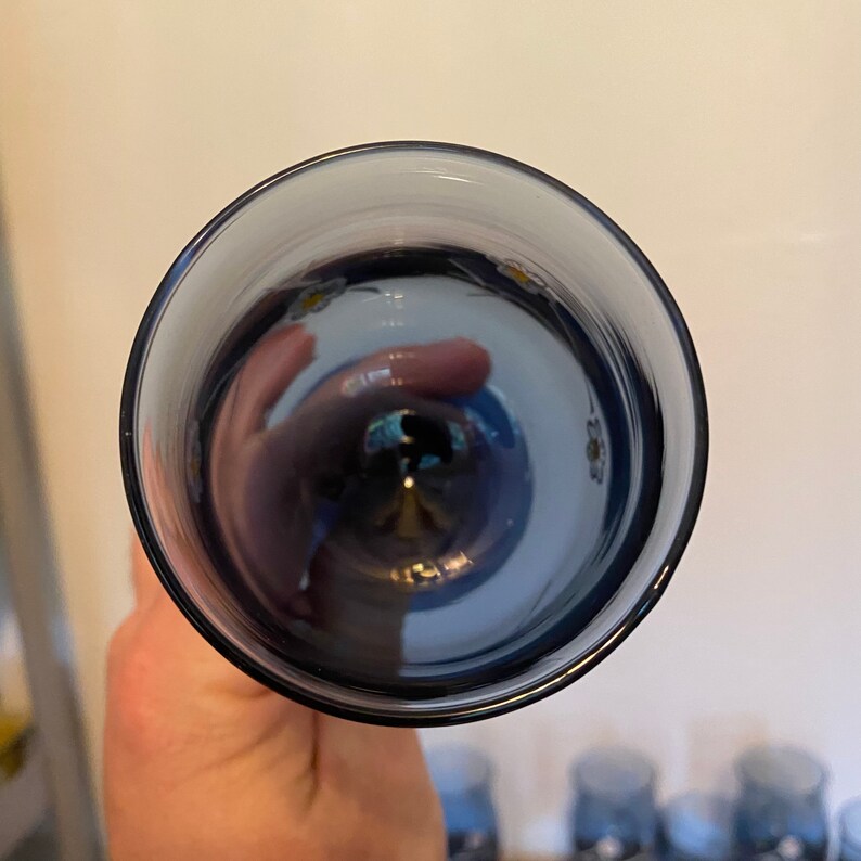 May include: A clear glass with a blue tint and a floral pattern on the inside. The glass is empty and appears to be part of a set.