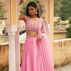 Featuring a pink lehenga in satin organza base with embroidery. It is paired with a matching net embroidered blouse and an organza dupatta.
