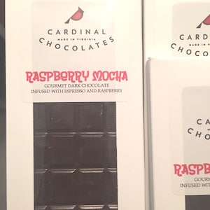 May include: A white box with a red cardinal logo and the text "CARDINAL CHOCOLATES MADE IN VIRGINIA"  The box contains a dark chocolate bar with the text "RASPBERRY MOCHA GOURMET DARK CHOCOLATE INFUSED WITH ESPRESSO AND RASPBERRY"