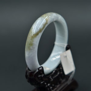 May include: A light blue jade bangle with a green and white swirl pattern. The bangle is on a black stand.