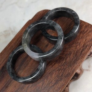 May include: Three black jade bangle bracelets stacked on a wooden stand. The bracelets are smooth and polished.