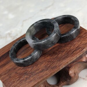 May include: Three gray jade rings stacked on a wooden stand. The rings are smooth and polished, with a subtle marbling effect.