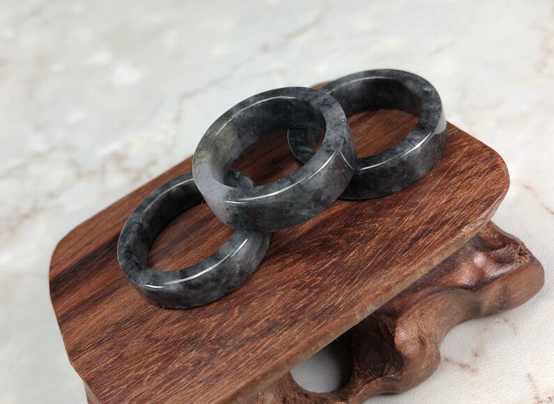 May include: Three gray jade rings stacked on a wooden stand. The rings are smooth and polished, with a subtle marbling effect.