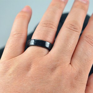 May include: A black ring worn on a person's finger. The ring is made of a smooth, dark material.