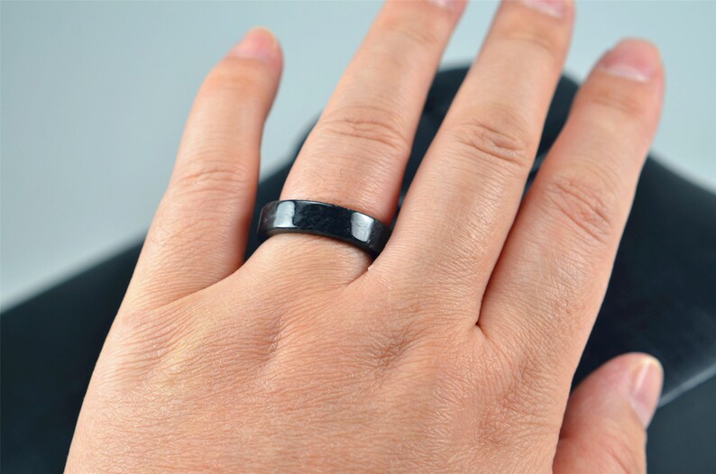 May include: A black ring worn on a person's finger. The ring is made of a smooth, dark material.