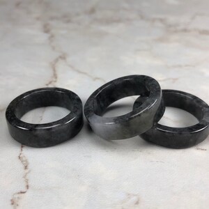 May include: Three black and gray jade rings stacked on a white marble surface.
