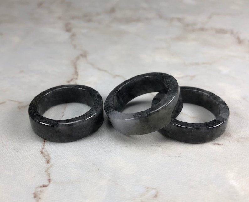 May include: Three black and gray jade rings stacked on a white marble surface.