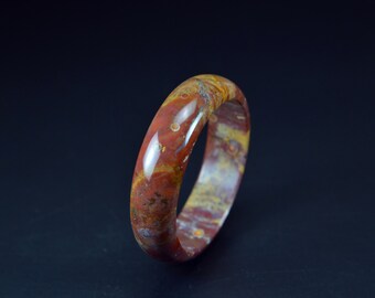 May include: A red, yellow, and white agate bangle bracelet. The bracelet is polished and has a smooth, glossy finish.