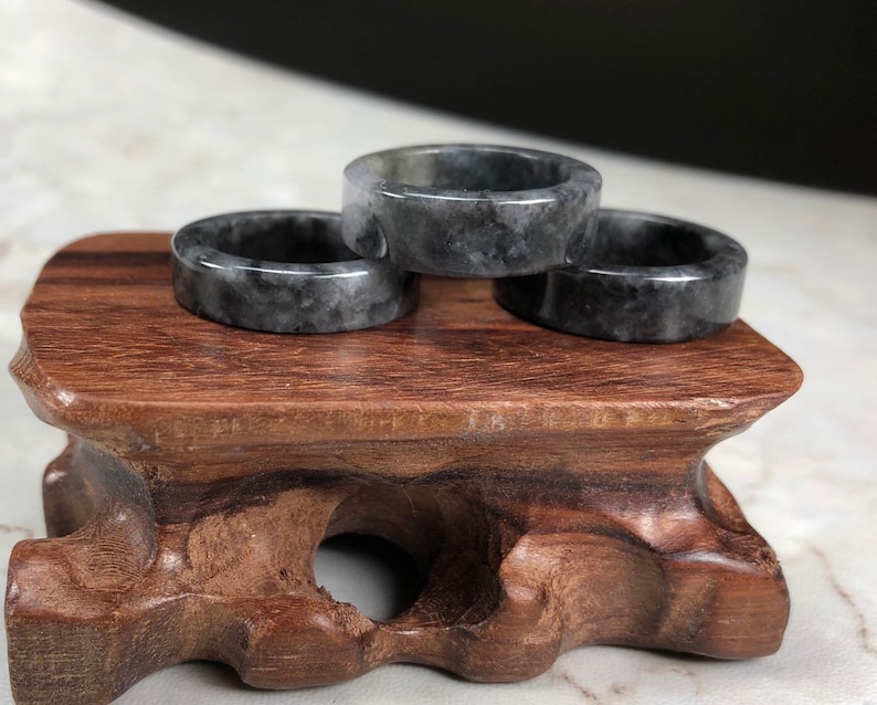 May include: Three dark gray jade rings stacked on a wooden stand. The rings are smooth and polished, with a subtle marbling effect.