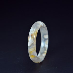 May include: A white agate ring with brown and yellow inclusions. The ring is smooth and polished.