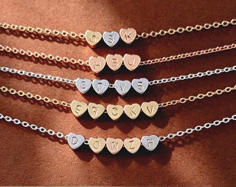 May include: Five delicate metal chain necklaces, each featuring a row of small heart-shaped charms. Each heart is engraved with a single uppercase letter. The necklaces are crafted in gold, rose gold, and silver tones, displaying various letter combinations.