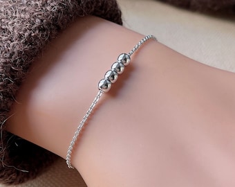 Peut inclure: Un bracelet argenté avec une chaîne délicate et quatre perles rondes.