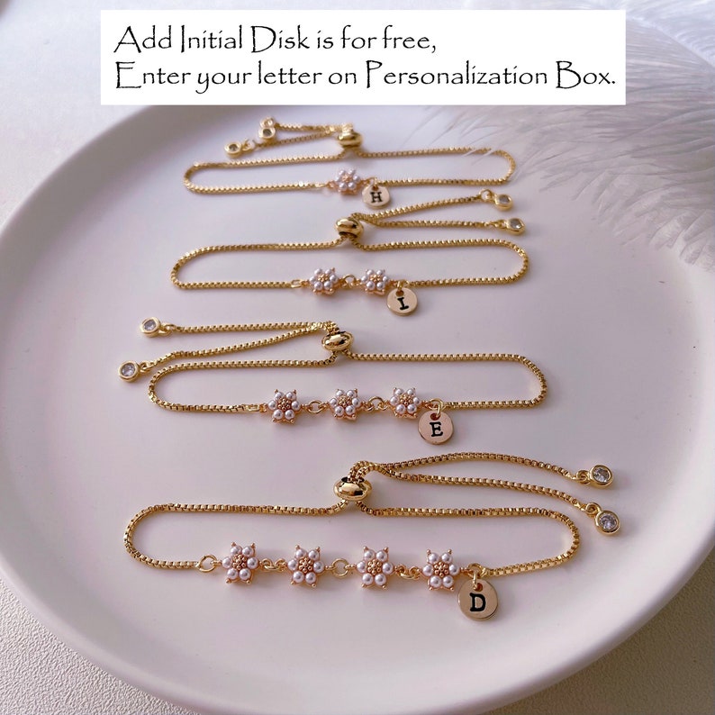 May include: Four gold chain bracelets with adjustable sliding knots. Each bracelet features a small gold disc with a letter charm, and a row of five small white flower charms. The letters on the charms are H, I, E, and D.