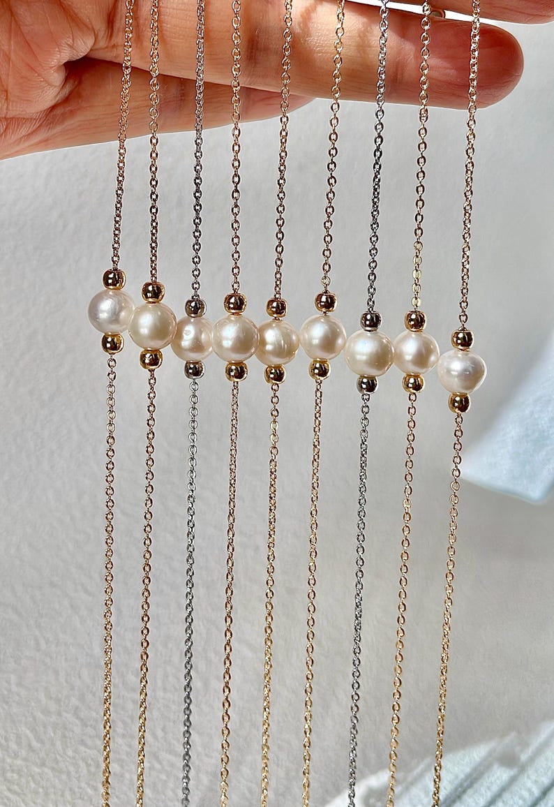 May include: A set of nine delicate necklaces featuring a chain with a row of five white pearls. The chains are in different metal finishes, including gold, silver, and rose gold.