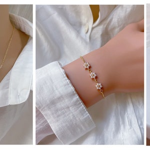May include: A set of delicate gold jewelry featuring a necklace, bracelet, and earrings with small pearl flower accents. The earrings are available in both stud and clip-on styles.