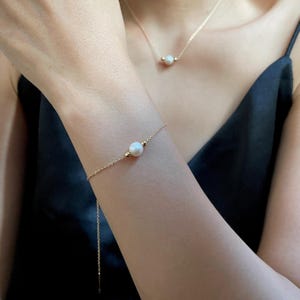May include: A delicate gold chain bracelet with a single white pearl charm. The bracelet is on a woman's wrist.