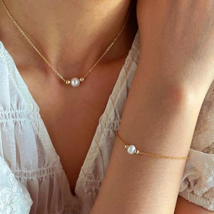 May include: A gold chain necklace and bracelet with a single pearl on each. The necklace and bracelet are both delicate and simple.
