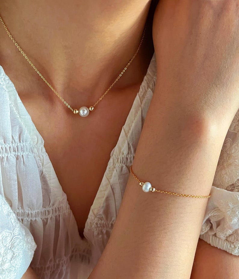 May include: A gold chain necklace and bracelet with a single pearl on each. The necklace and bracelet are both delicate and simple.