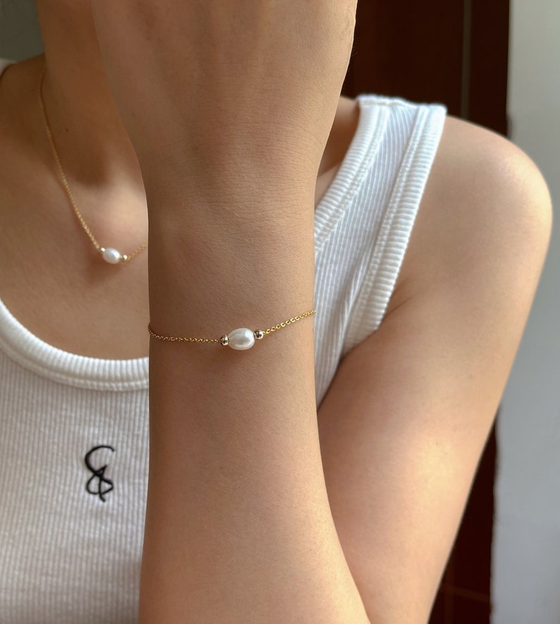 May include: A delicate gold chain bracelet with a single white pearl charm.