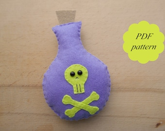 Puede incluir: Una botella de poción de fieltro morado con un diseño de calavera y huesos cruzados verdes. Patrón PDF.