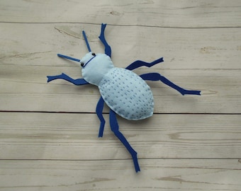 May include: A blue felt bug with blue legs and black eyes. The bug is stitched with white thread.