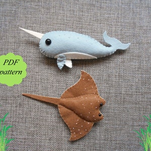 May include: A PDF pattern for sewing felt toys of a narwhal and a stingray. The narwhal is light blue with a white horn and white belly. The stingray is brown with white spots. The pattern is on a gray textured background.