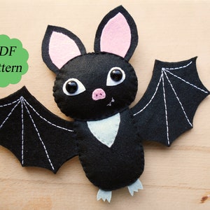 May include: A black felt bat with pink ears, white teeth, and black eyes. The bat has white stitching on its wings and is on a wooden surface. PDF pattern.