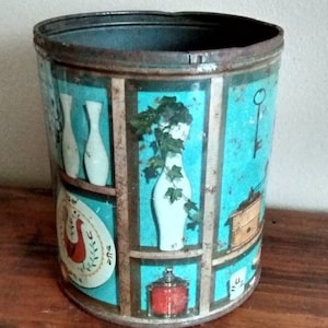May include: A vintage metal tin with a turquoise blue background and a colorful design featuring white vases, a key, and a bird. The tin has a rusty rim and is slightly dented.