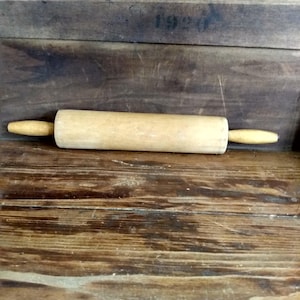 May include: A wooden rolling pin with light-colored handles and a cylindrical body. The rolling pin is made of light-colored wood and is designed for rolling out dough. The handles are a lighter shade of wood than the body.