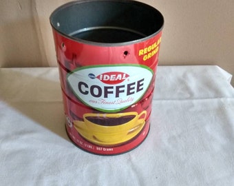 May include: A cylindrical red coffee can with the words "IDEAL COFFEE" in white and a yellow coffee cup graphic. The can has a black interior and the text "REGULAR GRIND". It contains 12 oz (340 grams) of coffee.