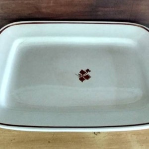May include: A white ceramic rectangular baking dish with a brown rim and a small brown floral design in the center.
