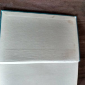 K&ouml;nnte beinhalten: Ein tealblaues Hardcover-Buch mit wei&szlig;em R&uuml;cken und wei&szlig;en Seiten. Das Buch ist geschlossen und liegt flach auf einer Holzoberfl&auml;che.
