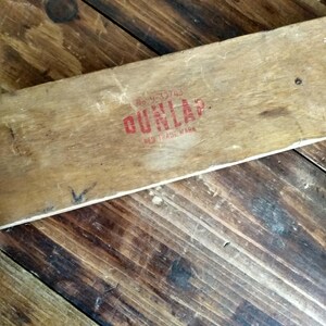 May include: A weathered wooden plank with the red text "DUNLAP RED TRADE MARK" stamped on it. The plank is set against a backdrop of a wooden surface with a diagonal pattern.