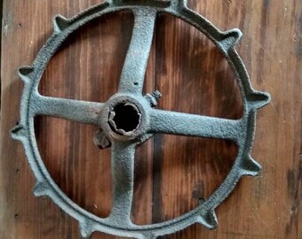 May include: A rusty metal wheel with a central hub and spokes. The wheel has a series of teeth around the outer edge.