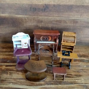 May include: A collection of miniature wooden dollhouse furniture including a white cabinet, a brown upright piano, a roll-top desk, a purple chair, a sewing machine on a table, a round stool with heart carvings, and a small rectangular wooden stool.