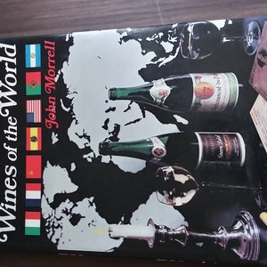 May include: A book cover with a black background and a world map. The title is "Wines of the World" and the author is "John Morrell". There are images of wine bottles and glasses on the cover.