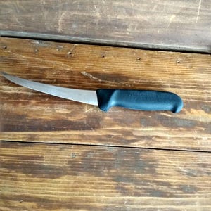 May include: A stainless steel fillet knife with a curved blade and a black handle. The handle has the brand name "Victorinox" printed on it. The knife is designed for precision cutting and is suitable for preparing fish or other meats.