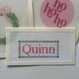 May include: White canvas with a green and white border, the name "Quinn" is written in pink letters inside the border.
