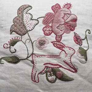 May include: Embroidered design featuring a pink and green floral motif with a white rabbit hopping through the flowers.
