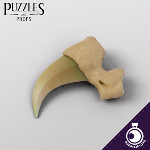 May include: A beige and green plastic claw prop. The claw is curved and sharp, with a textured surface.