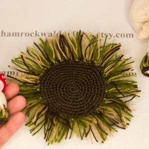May include: A brown crocheted sunflower with green and beige yarn fringe. The sunflower is approximately 10 cm in diameter.