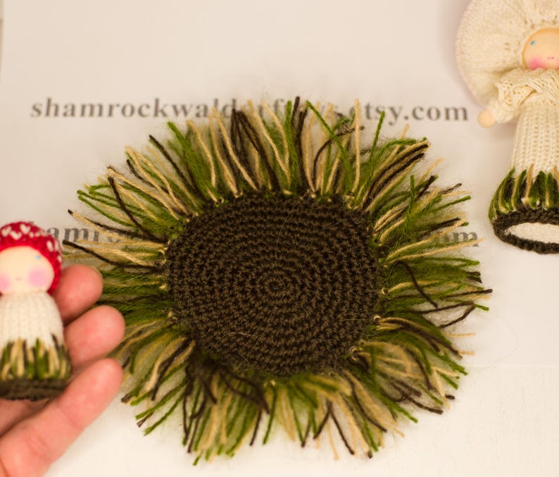 May include: A brown crocheted sunflower with green and beige yarn fringe. The sunflower is approximately 10 cm in diameter.