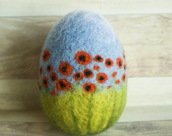 May include: A blue and green felt Easter egg with a design of red poppies on a field of green grass.