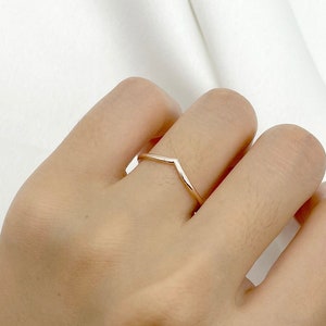 May include: A simple gold-toned ring with a V-shaped design. The ring is worn on a finger.